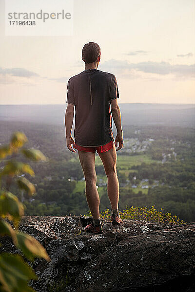 Erwachsener männlicher Trailrunner beim Klettern auf einem Bergkamm bei Sonnenuntergang
