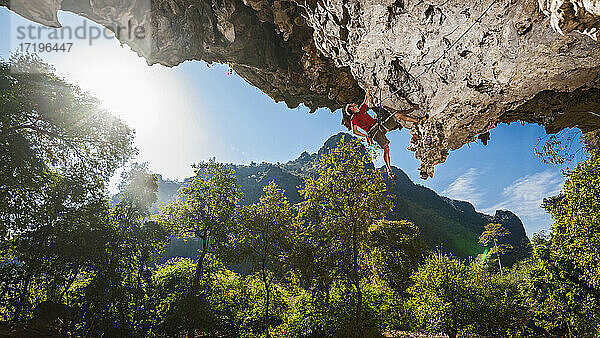 Mann klettert auf überhängendem Kalksteinfelsen in Laos