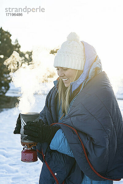 Lächelnde Frau mit Campingkocher im Winter