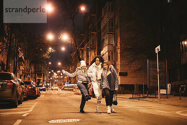 Glückliche weibliche Freunde haben Spaß auf der Straße in der Stadt in der Nacht zu Fuß