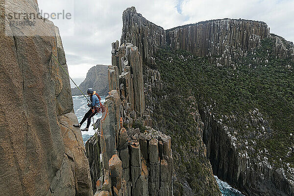 Eine Bergsteigerin schaut nach unten  während sie sich an einem Seil vom Rand einer Meeresklippe abseilt  um die Doleritsäulen von Cape Raoul  Tasmanien  Australien  weiter zu erforschen.