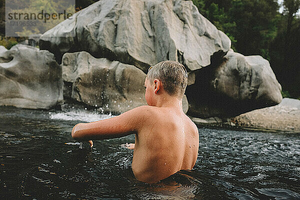 Junge mit nasser Haut steht in einem dunklen Pool  in dem das Wasser um ihn herum wirbelt