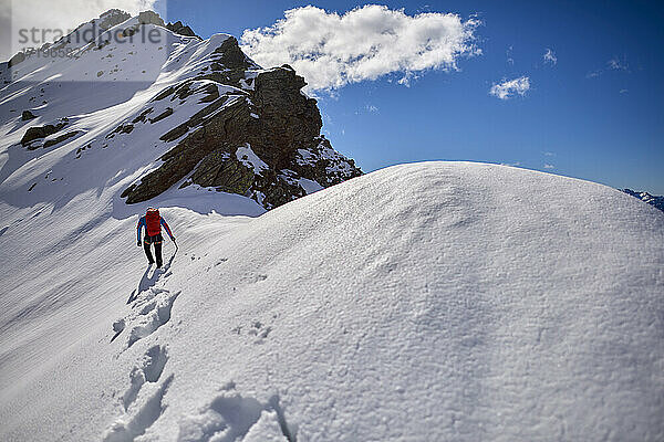 Ein Mann besteigt an einem sonnigen Tag einen verschneiten Berg in Devero  Italien.