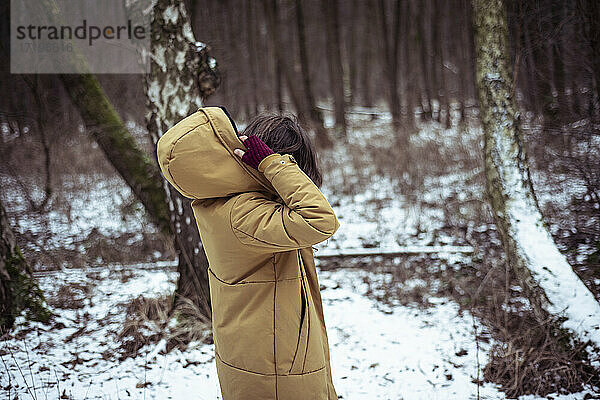 Person setzt Kapuze auf Wintermantel draußen im verschneiten Wald