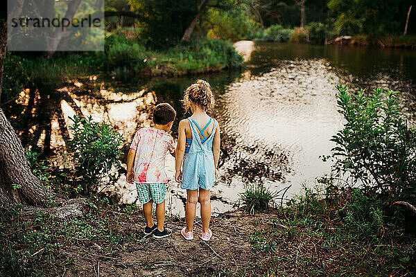 Zwei junge Kinder stehen am Rande eines Sees und zeigen auf Fische im Wasser
