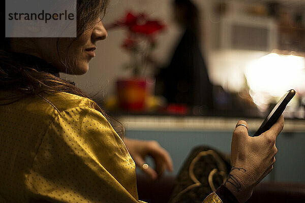Frau in goldenem Seidenhemd zu Hause gemütliche Küche schaut auf Telefongerät