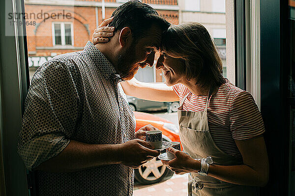 Junges verliebtes Paar trinkt Kaffee und lächelt  während es vor der Tür steht