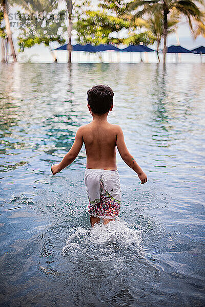 Ein Junge  der in einen Infinity-Pool in einer tropischen Umgebung geht.