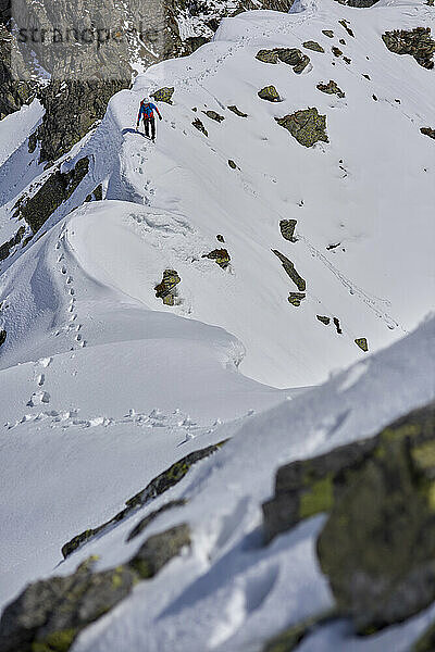 Ein Mann besteigt an einem sonnigen Tag einen verschneiten Berg in Devero  Italien.