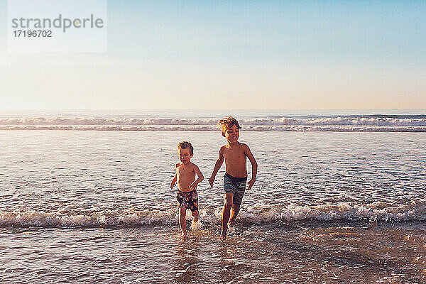 Zwei Jungen laufen am Strand im Wasser.