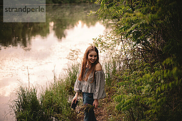 Glückliches Teenager-Mädchen  das im Sommer am Fluss im Wald steht