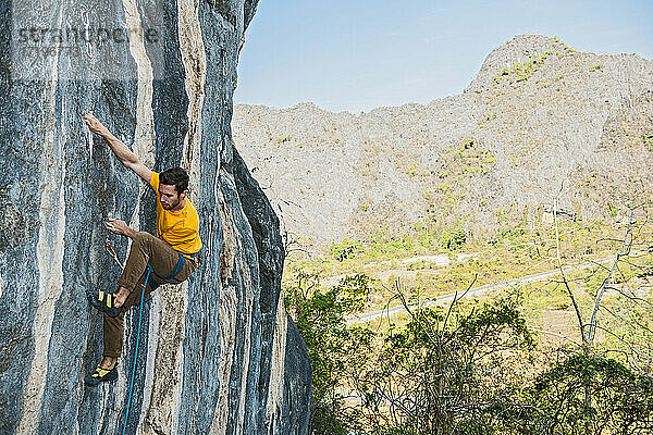 Mann klettert auf Kalksteinfelsen in Laos