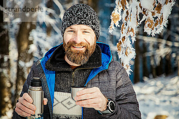Mann trinkt heißen Tee im Winterwald