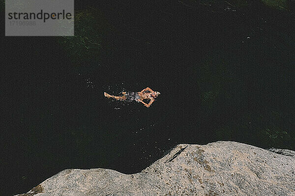 Vogelperspektive eines Jungen  der im dunklen Wasser auf dem Rücken schwimmt