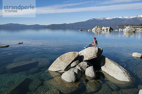 junge frau sitzt auf felsen im lake tahoe an einem sonnigen nachmittag