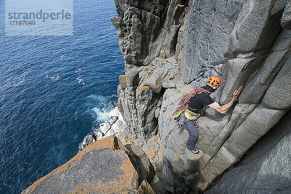 Ein männlicher Abenteurer macht sich auf den Weg ins Unbekannte  bewaffnet mit Seilen und Kletterausrüstung  um Dolerit-Felssäulen in den Meeresklippen von Cape Raoul in Tasmanien  Australien  zu erforschen.