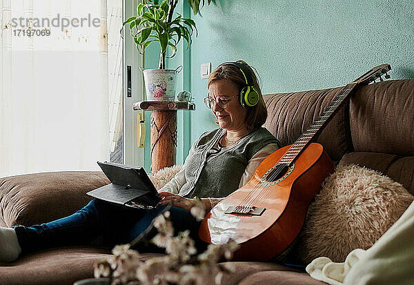 Frau mittleren Alters mit Kopfhörern lernt zu Hause Gitarre spielen
