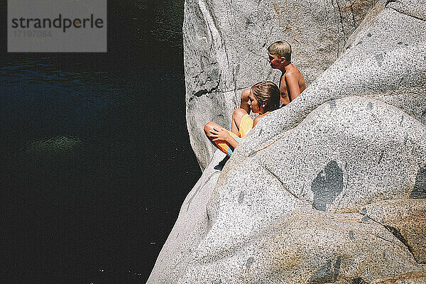 Zwei Jungen sitzen in der Sommersonne über dem dunklen Wasser unter ihnen