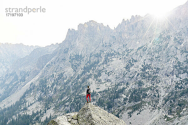 Rückansicht einer Frau  die beim Wandern auf einem Felsen vor einem Berg steht