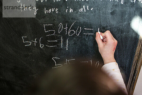 Nahaufnahme eines kleinen Kindes  das mathematische Gleichungen auf eine Kreidetafel schreibt