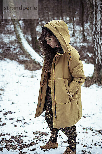 Junge Frau mit Sommersprossen und langen lockigen Haaren lächelt unter der Kapuze im Schnee