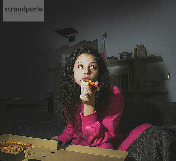 junge Frau isst Pizza auf dem Sofa und sieht sich einen Film an
