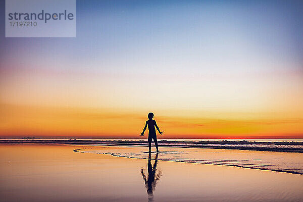 Silhouette eines Jungen  der am Strand in der Abenddämmerung im Wasser spielt.