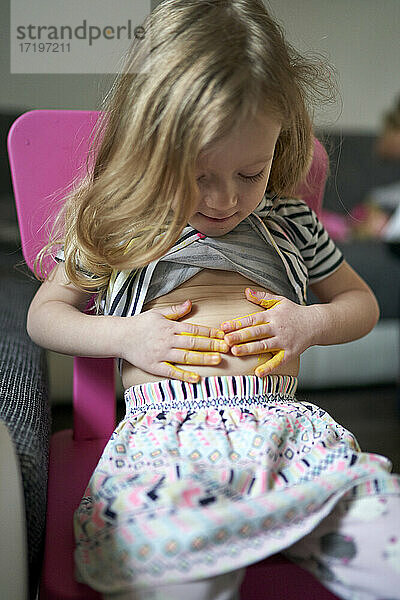 Nettes glückliches kleines Mädchen Künstler Druck gelb gemalt Palmen auf ihrem Bauch.