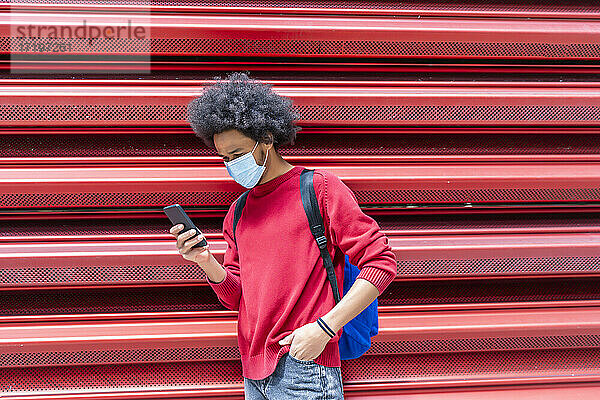 junger Mann mit Afro-Haar  der eine Nachricht von seinem Smartphone sendet