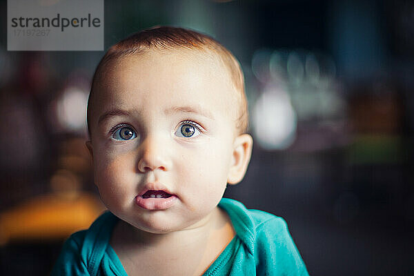 Baby mit haselnussbraunen Augen und grünem Strampler.