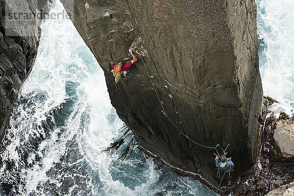 Ein Felskletterer greift nach einer Kräuselung  als er einen Felsen aus dem Ozean in The Totem Pole  Cape Hauy  Tasman National Park  Tasmanien  Australien  erklimmt.