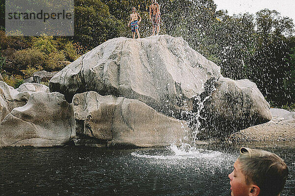 Freunde werden nach einem Sprung nass. Big Splash am Schwimmloch in der Abenddämmerung