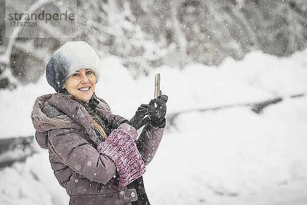 Frau mit Schneemütze macht ein Selfie mitten im Schneefall