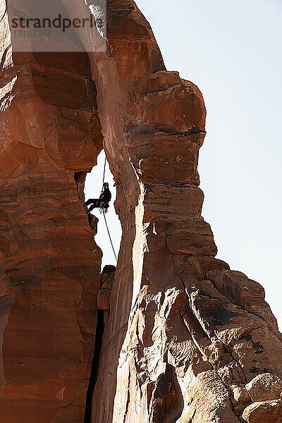 Niedriger Blickwinkel eines Mannes  der auf Felsen klettert  gegen den klaren Himmel im Canyonlands National Park