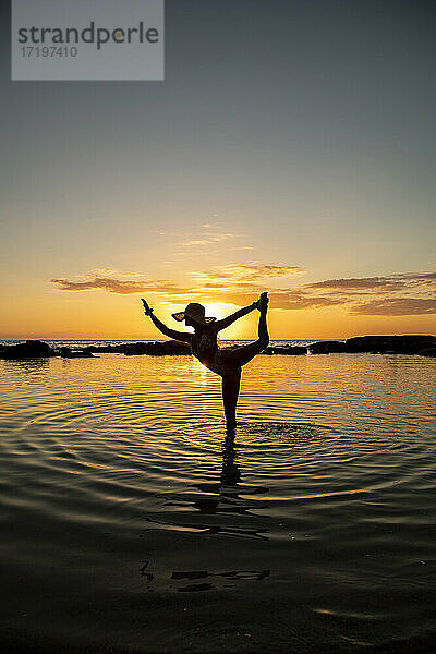 Frau in Tänzerin Pose im flachen Wasser vor Sonnenuntergang
