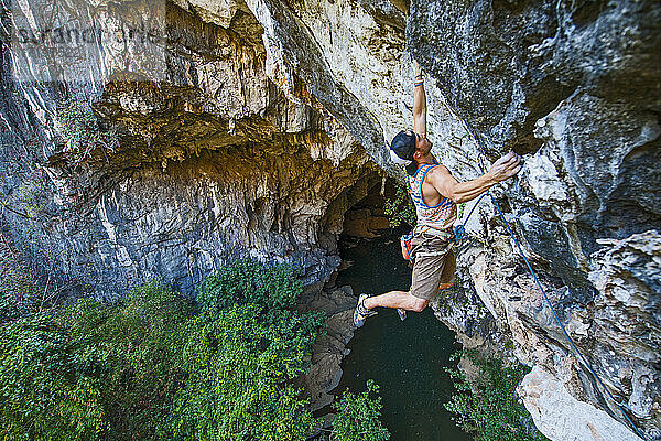 Mann klettert auf überhängendem Kalksteinfelsen in Laos