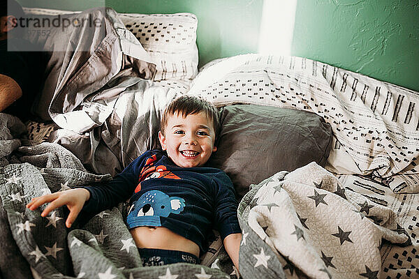 Junge im Schlafanzug im Bett lächelnd und in die Kamera schauend