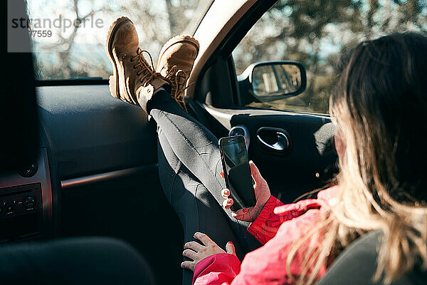 Ein abenteuerlustiges Mädchen sitzt im Auto und konsultiert ihr Mobiltelefon  um in Verbindung zu bleiben.