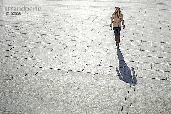 Blonde Frau mit rosa Mantel beim Treppensteigen