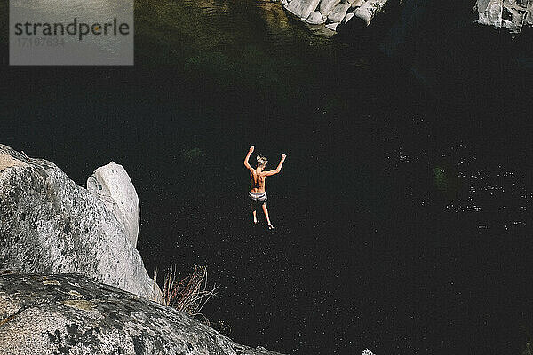 Teenager-Junge springt von hoher Klippe in dunkles Wasserbecken