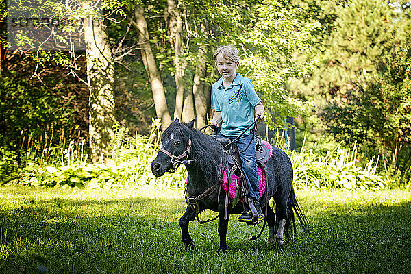 Der kleine Blonde reitet auf seinem kleinen schwarzen Pony durch die Landschaft.