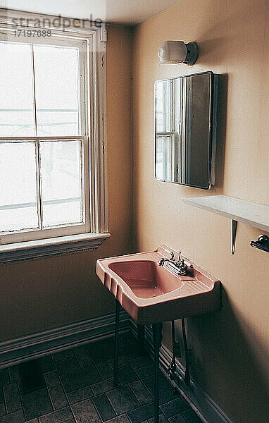 Rosa Waschbecken und Spiegel im Retro-Stil in einem alten  leeren  schmuddeligen Badezimmer.