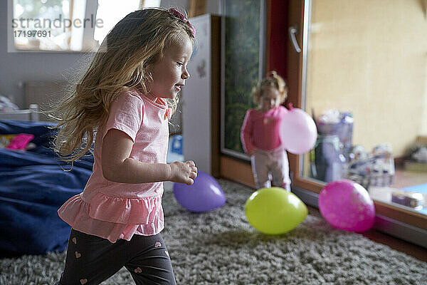 Fröhliches kleines Mädchen  das zu Hause herumläuft und mit seiner Schwester und den Ballons spielt.