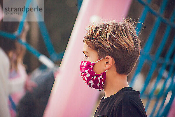 Junge mit Maske spielt allein auf einem rosa Spielplatz