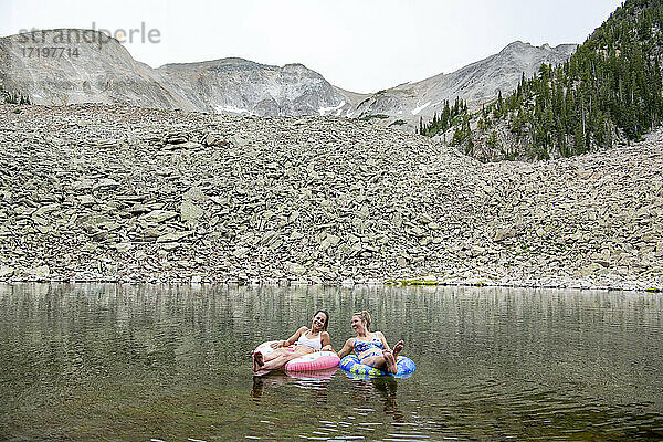 Glückliche Freundinnen sitzen auf aufblasbaren Ringen in einem See im Urlaub