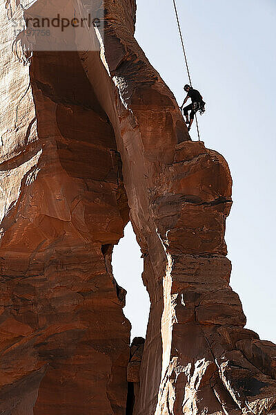 Niedriger Blickwinkel eines Mannes  der auf Felsen klettert  gegen den klaren Himmel im Canyonlands National Park