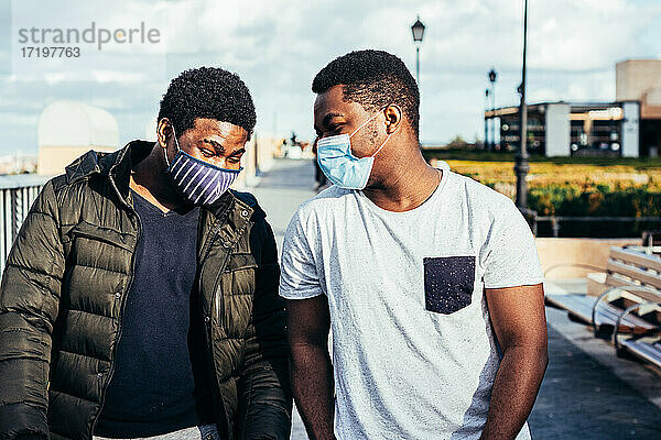 Porträt von zwei afroamerikanischen Freunden mit Gesichtsmaske  die sich in einem städtischen Raum amüsieren.