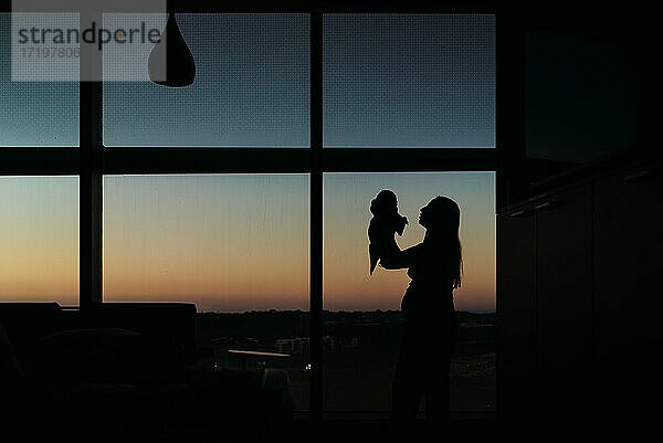 Silhouette von Mutter und Neugeborenem im Krankenhauszimmer bei Sonnenuntergang