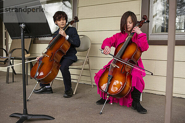 Ein Junge mit einem Cello schaut zu  während seine Schwester ihr Instrument spielt