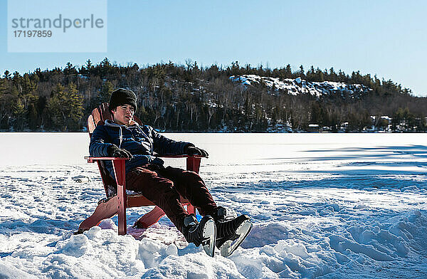 Teenager  der an einem Wintertag eine Pause vom Schlittschuhlaufen auf einer Eisbahn im Freien macht.